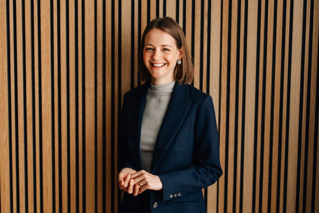 Gesa Zoetler in a suit standing in front of a wooden wall
